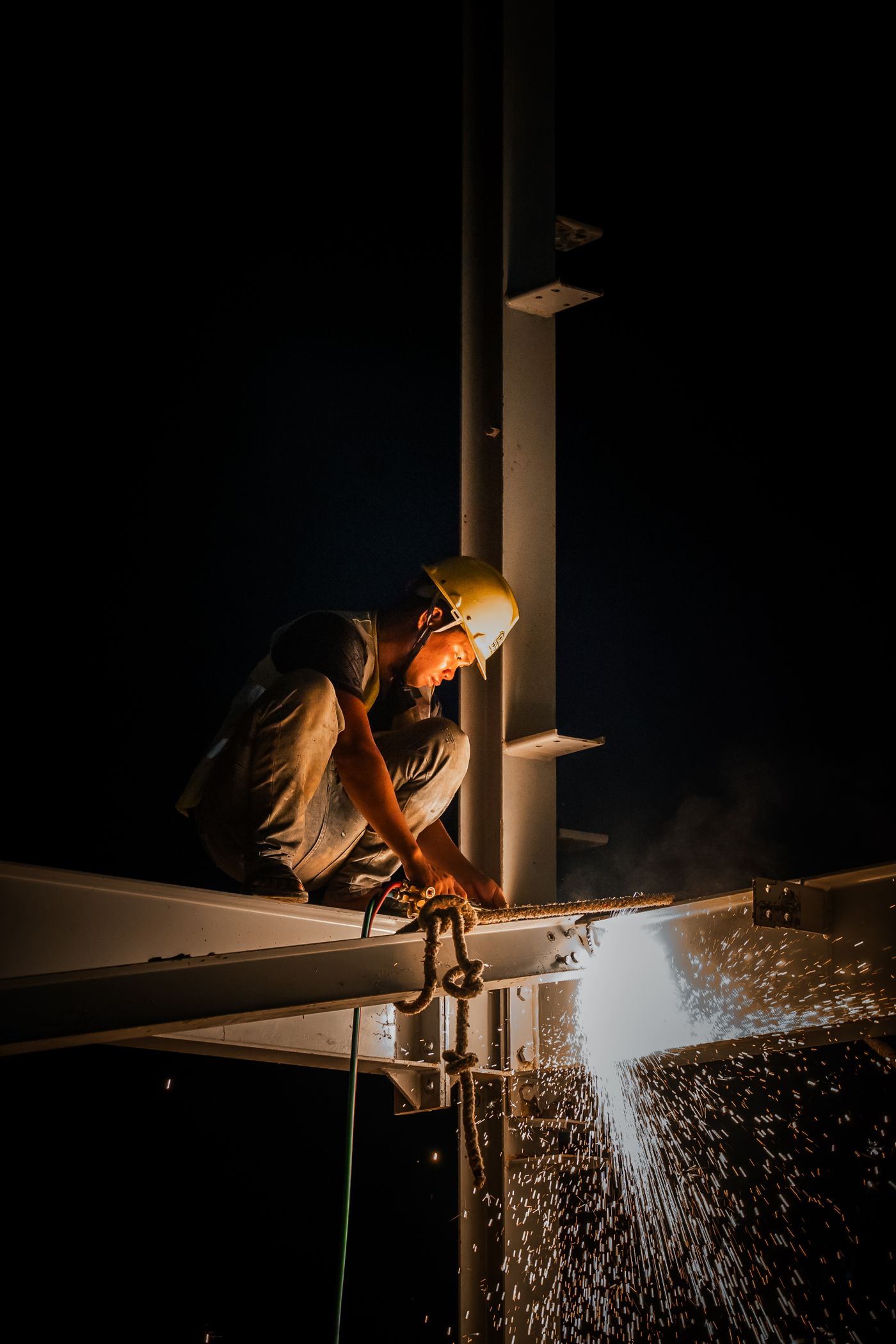 Lasser aan het werk aan een stalen constructie, vonken in het donker.