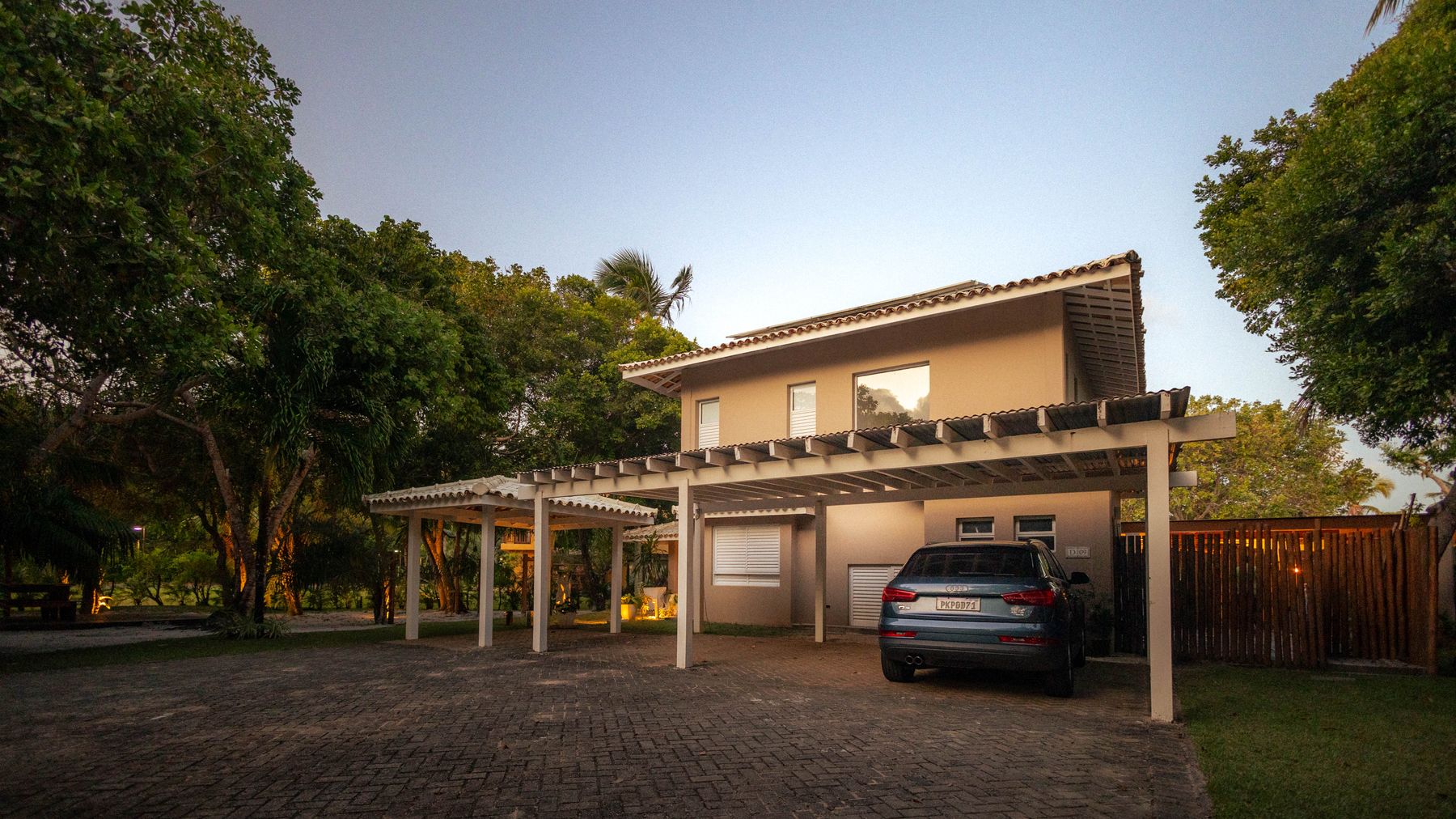 Woning met houten overkapping, carport en bestrating in de avondschemering.