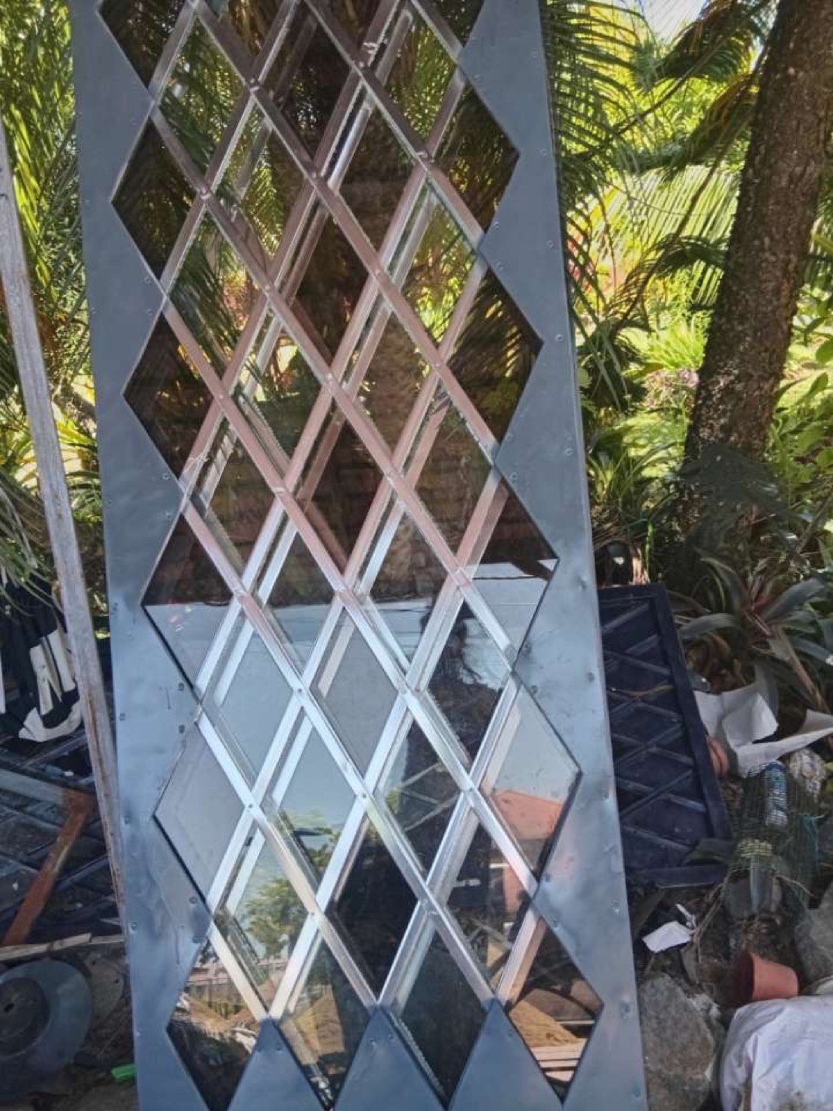 Stalen designdeur met ruitvormig glasmotief, klaar voor montage, opgesteld in de tuin.